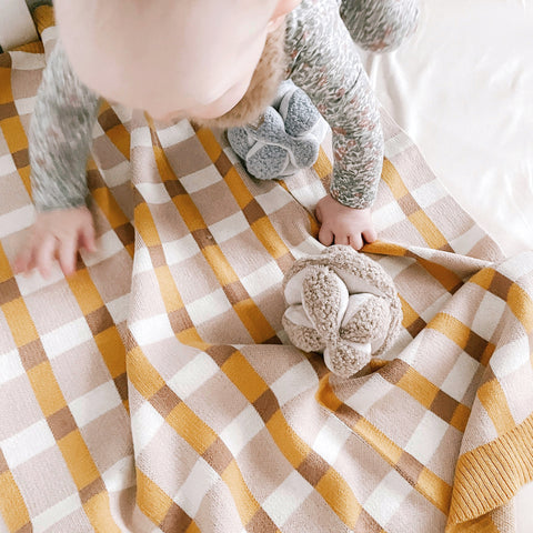 Baby crawls on a soft yellow and beige gingham blanket with two plush sensory toys.
