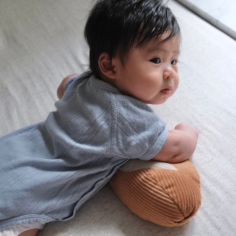 Baby practices tummy time while propped on a textured, brown pillow.