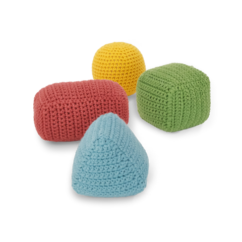 Four crocheted baby blocks form a colorful pyramid: a blue pyramid, a red rectangle, a yellow sphere, and a green cube.