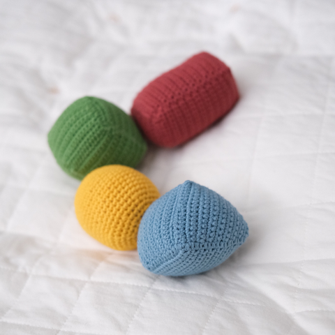 Four colorful crocheted toys rest on a white quilted blanket.
