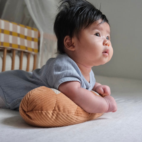 Curious baby lifts head to look up while lying on a brown corduroy pillow.