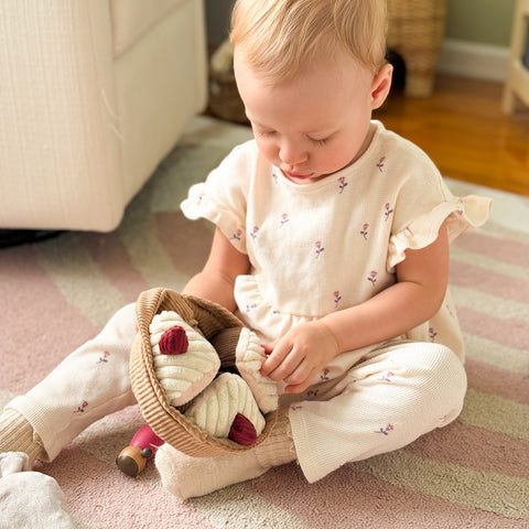 Baby girl plays with plush toy cupcakes in a corduroy basket.