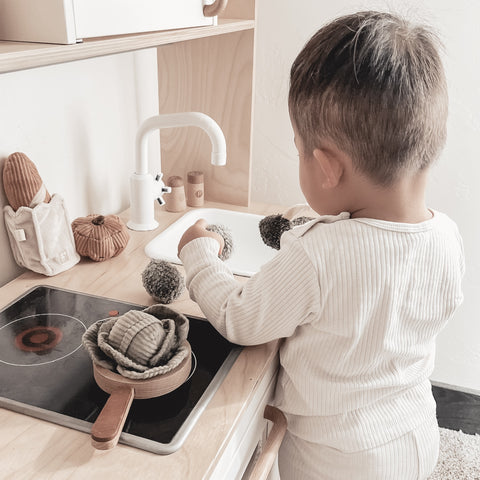 Toddler plays with toy food on a wooden play kitchen.