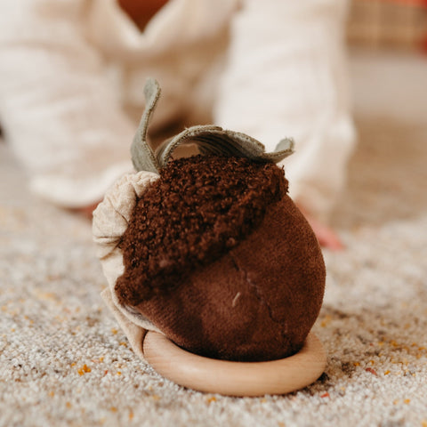 Handmade felt acorn toy with wooden teething ring resting on a soft, textured rug.