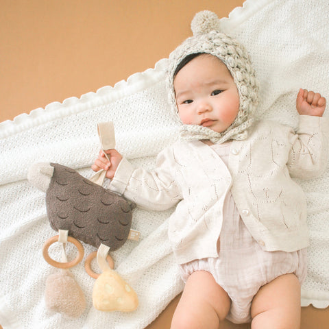 Baby explores textures on a soft blanket, gripping a wooden teething toy shaped like a friendly llama.