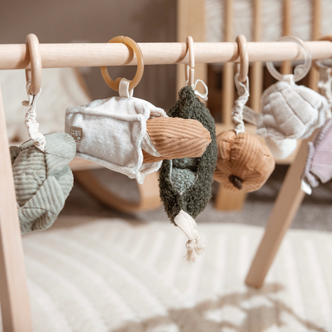 Wooden baby gym hangs with plush vegetable toys in muted greens and tans.