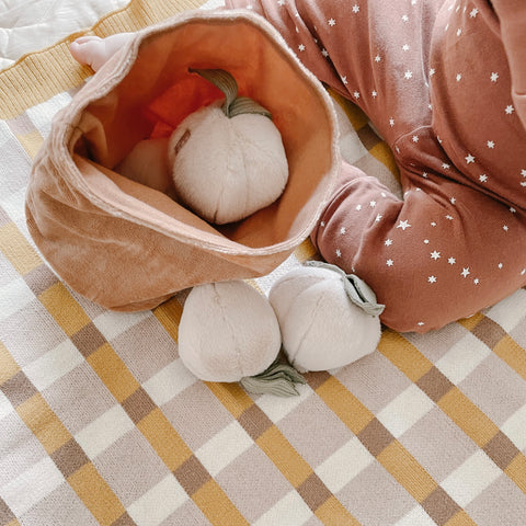 Baby plays with plush peach toys on a yellow and brown gingham blanket.