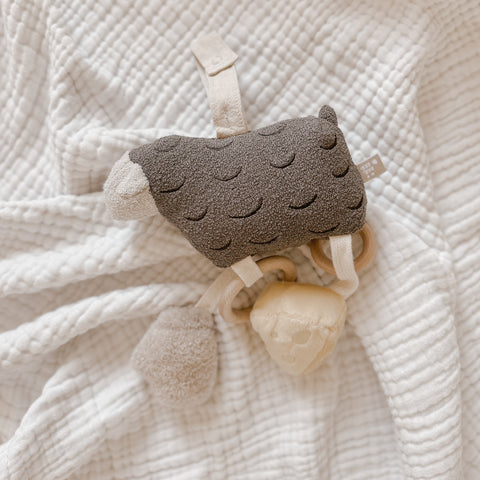 Soft, textured llama toy lays on a white blanket. The llama is brown with a cream underbelly and features wooden rings for gripping.