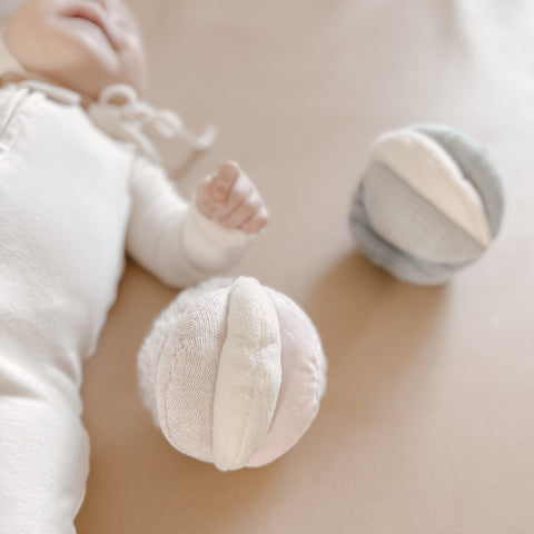 Baby holds soft, pastel-colored fabric ball during tummy time.