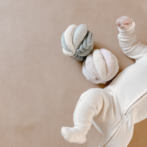 Baby kicks feet in the air while playing with two soft, pastel-colored sensory balls.