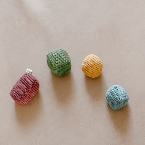 Four colorful crocheted baby rattle toys rest on a soft, beige surface.