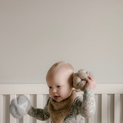 Smiling baby plays with knitted toys in a crib.