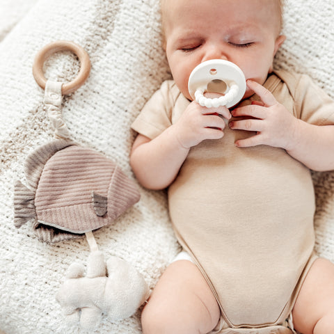Sleeping baby relaxes on a soft blanket while holding a textured teething ring.