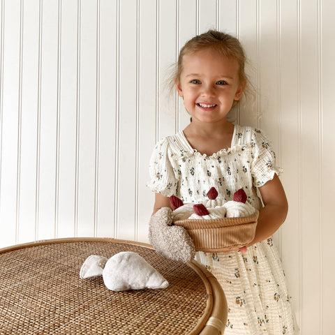 Smiling young girl holds a basket of plush toy turnips and wears a plush toy turnip oven mitt.