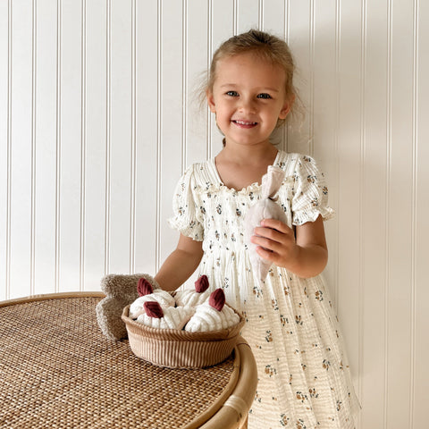 Smiling young girl displays a basket of plush toy pastries and a matching grocery bag.