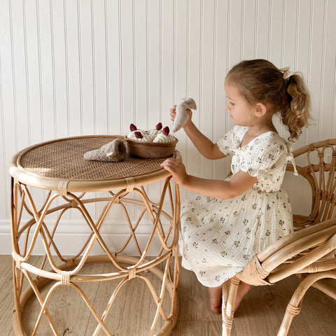 Young girl places a toy pastry onto a rattan side table during pretend play.