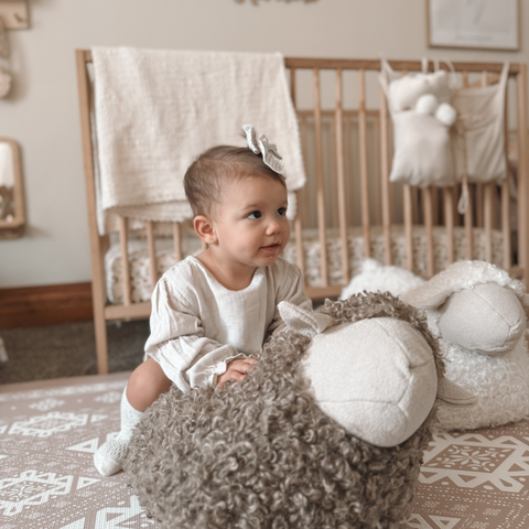Curious baby girl plays with a fluffy sheep toy in a cozy nursery.