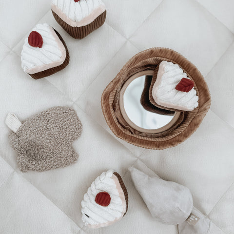 Plush toy cake slices and ice cream cone surround a corduroy-covered baby-safe mirror on a white quilted play mat.
