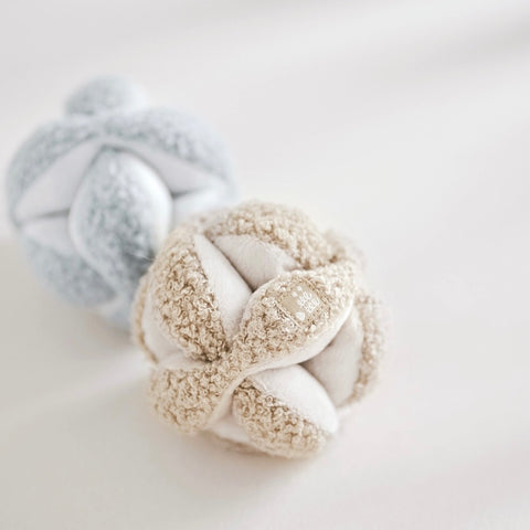 Two soft, plush baby toys shaped like knotted balls rest on a white blanket.