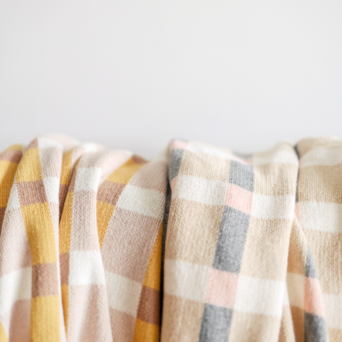 Two cozy plaid blankets in yellow, pink, gray, and cream create a comforting background.