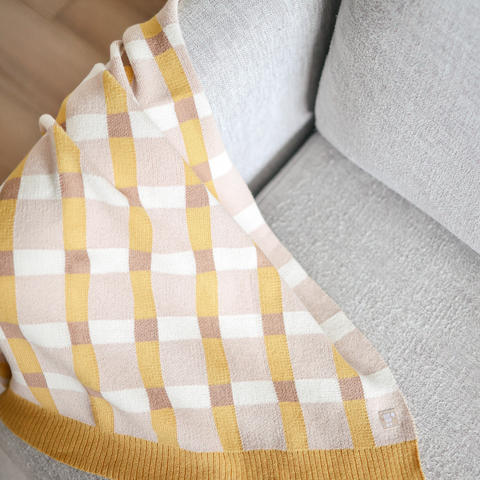 Soft yellow, cream, and tan checkered throw blanket draped over a gray armchair.