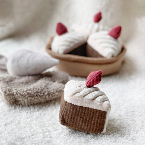 Plush chocolate cake toy with white frosting and a red strawberry sits on a fluffy white rug.