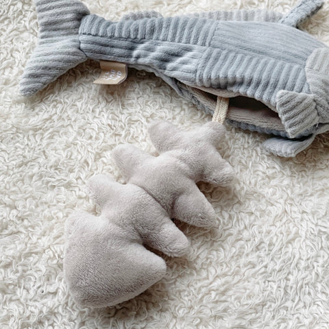 Gray corduroy whale rattle toy lays on a white sherpa blanket.
