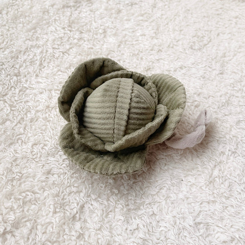 Plush green cabbage toy with corduroy texture rests on a soft, white rug.